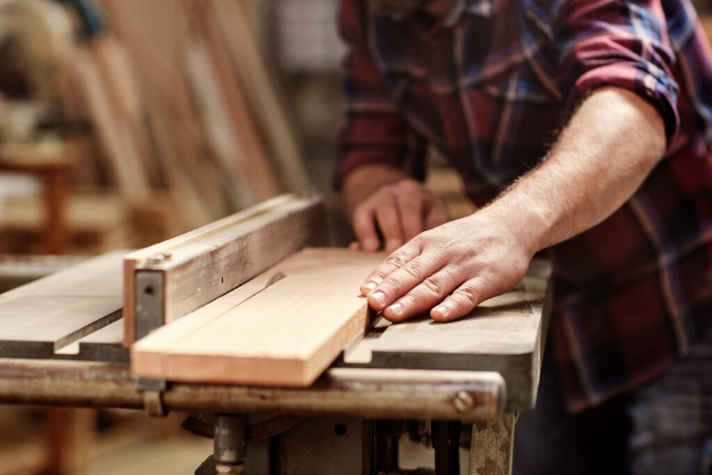 Cropped image of the hands of a skilled craftsman cutting a wooden plank with a circular saw in a workshop. Characteristics of Wood